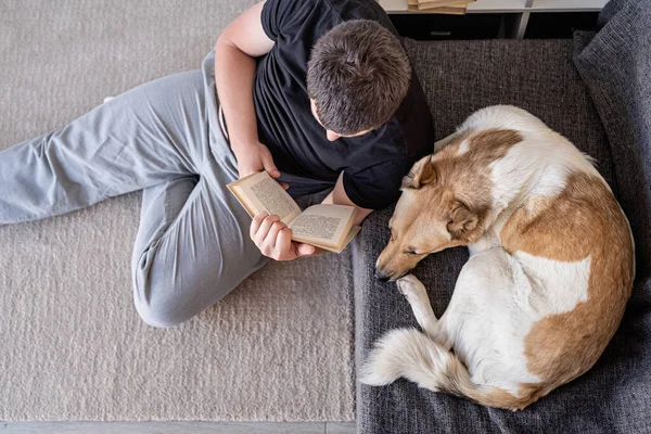 Joven leyendo sentado en el suelo en casa con su perro — Foto de Stock