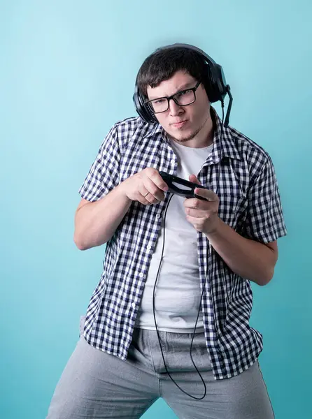 Zabawny młody człowiek gra w gry wideo trzymając joysticka na niebieskim tle — Zdjęcie stockowe