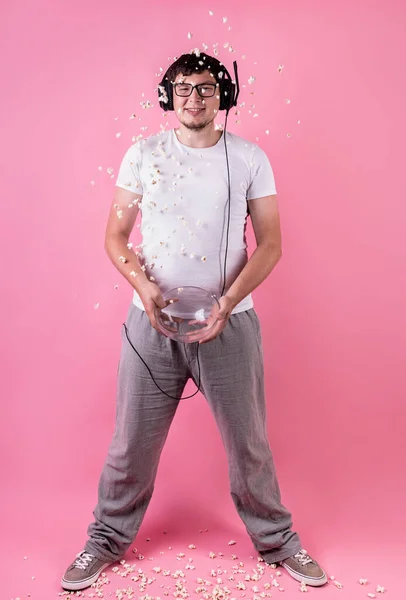 Joven hombre sonriente lanzando palomitas de maíz en el aire aislado en rosa — Foto de Stock