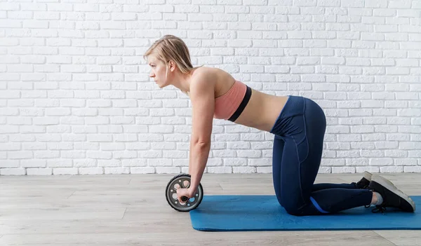 woman with slim stomach doing abdominal exercises with gymnastic roller