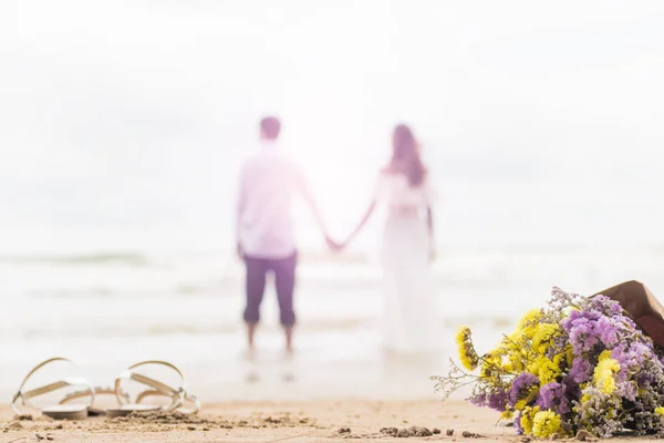 Buquê de flores na praia com casal desfocado backgroun brilhante — Fotografia de Stock