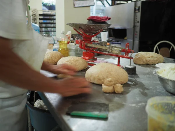 Man is rolling buns from raw dough. Sweet bread making process in a local bakery