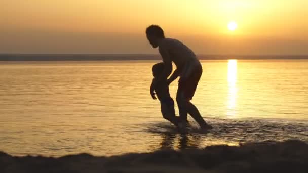 Pai e filho brincando na praia na hora do pôr do sol. Conceito de família amigável — Vídeo de Stock