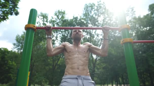 Ung man gör pull ups på vågräta fältet utomhus — Stockvideo