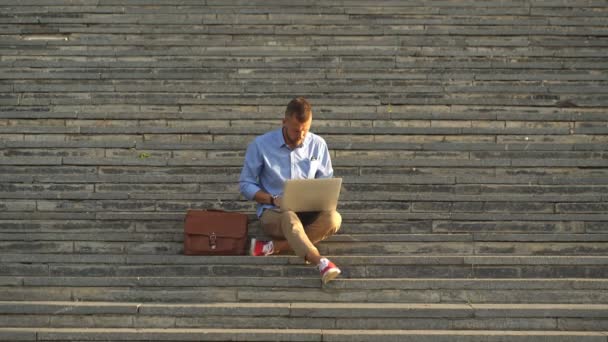 Sidovy av ung Man sitter på trappan i parken med hjälp av bärbar dator — Stockvideo