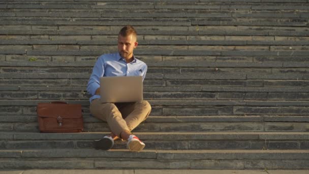 Homme d'affaires attrayant assis sur un campus universitaire avec ordinateur portable. Éducation technologie mode de vie . — Video