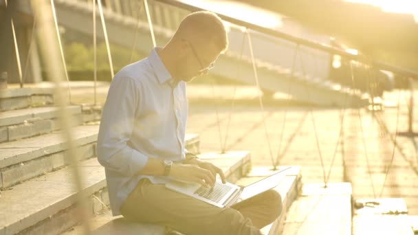 Étudiant heureux naviguant sur Internet sur son ordinateur portable et assis en plein air — Video