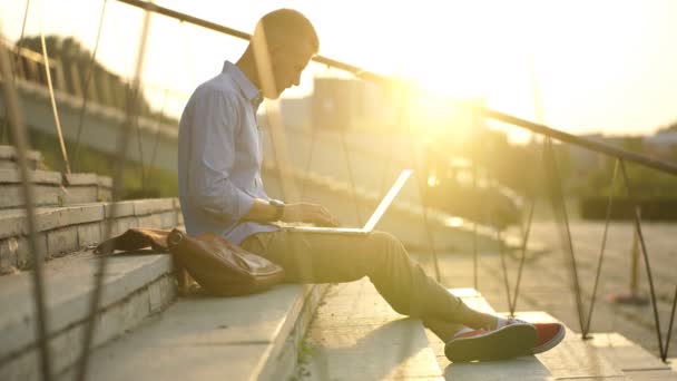 Uomo d'affari hipster con computer portatile si siede sulle scale e lavora al tramonto — Video Stock