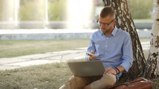 Knappe hipster met behulp van laptop in park op een zomers dag — Stockvideo