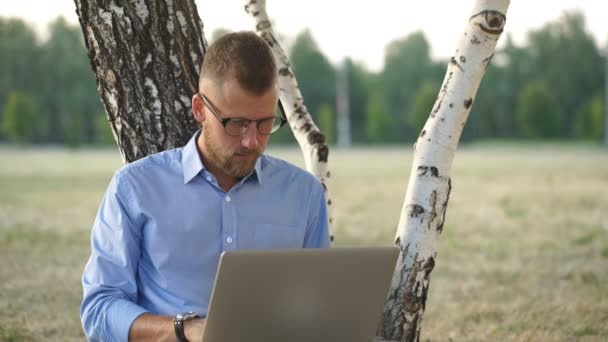 Homem está sentado no parque, sentado no chão, trabalhando com Laptop Freelance — Vídeo de Stock