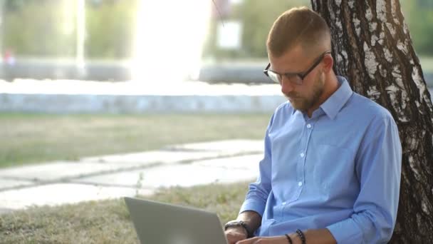 Bonito hipster usando laptop no parque em um dia de verão — Vídeo de Stock
