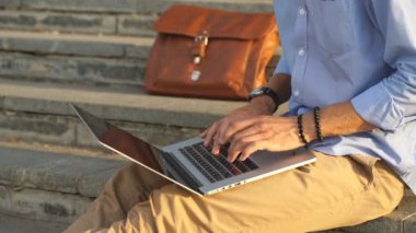 Ayrıntı merdivenlerde oturan ve dizüstü bilgisayar kullanarak modern hipster adam ayak