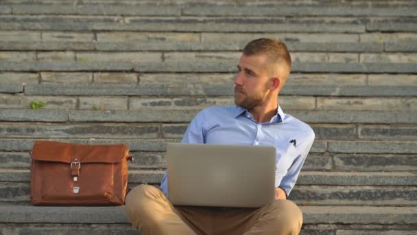 Молодий чоловік сидить на сходах за допомогою ноутбука — стокове відео