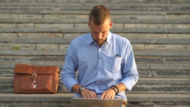 Jongeman zit op de trappen met behulp van laptop — Stockvideo