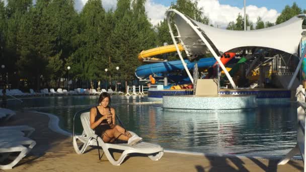 Chica bebiendo jugo en una tumbona junto a la piscina — Vídeos de Stock