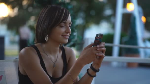 Beautiful woman sitting in a cafe at sunset and typing the message — ストック動画