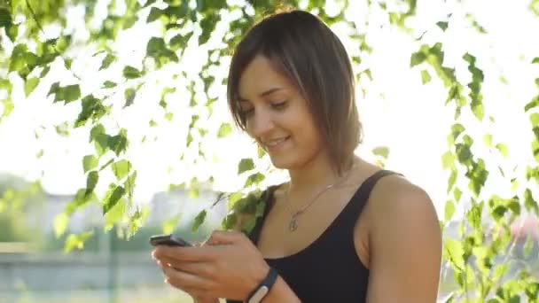 Красивая женщина, печатающая сообщение на телефоне в парке — стоковое видео