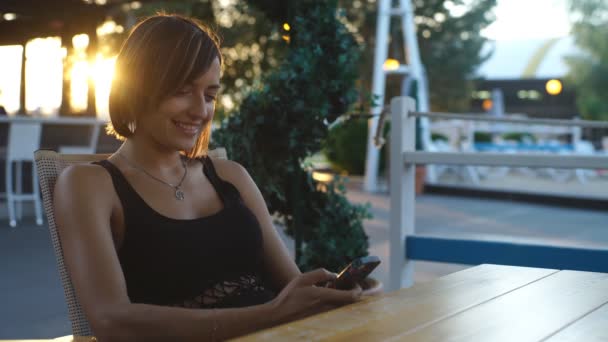 Beautiful woman sitting in a cafe at sunset and typing the message — Αρχείο Βίντεο
