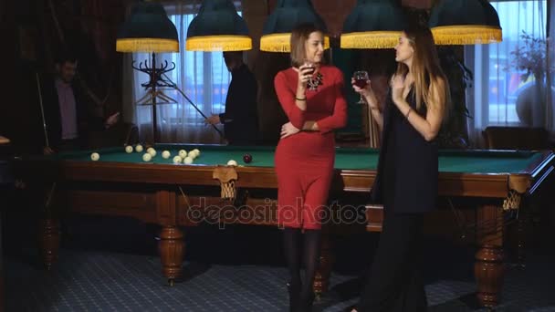 两个漂亮的女人站在旁边一张台球桌和两个男人在打台球的背景聊天 — 图库视频影像