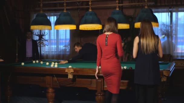 Two beautiful women standing near a pool table talking to two men in the background playing pool — Stock Video