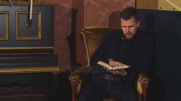 Muž sedí v křesle a čte si knihu — Stock video