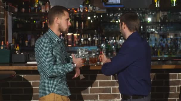 2 つの若い男は、カウンターで話しています。立っている 2 人の友人バーし、ウイスキーを飲む — ストック動画
