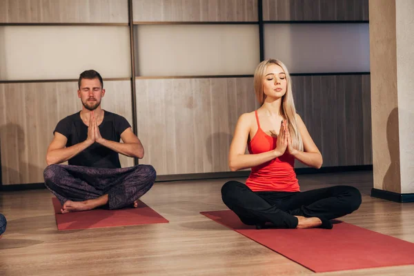 Pareja joven haciendo ejercicios de yoga en el gimnasio — Foto de Stock