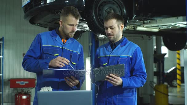 Dos mecánicos con una tableta que registra la información de diagnóstico del coche — Vídeos de Stock