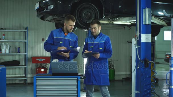 Dois mecânicos com um tablet que registra as informações de diagnóstico do carro — Vídeo de Stock