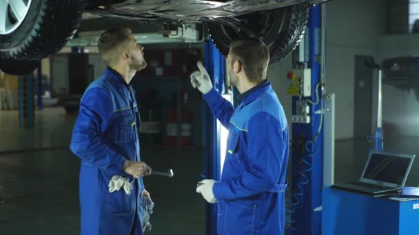 Fröhliche junge Mechaniker gestikulieren, während sie vor dem Auto stehen und in die Kamera lächeln — Stockvideo