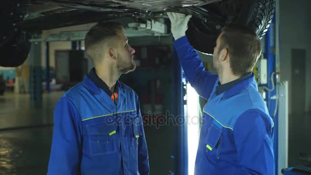 Vrolijke jonge mechanica gebaren terwijl voor de auto staan en lachend op camera — Stockvideo