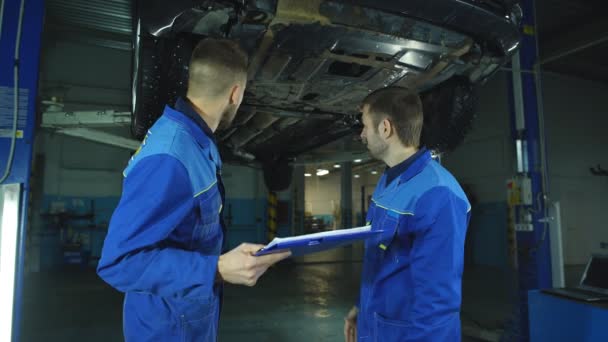 Mechanik i praktykant pracujący pod samochód — Wideo stockowe