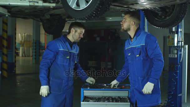 Jóvenes empleados del taller trabajando juntos debajo de un coche levantado — Vídeo de stock