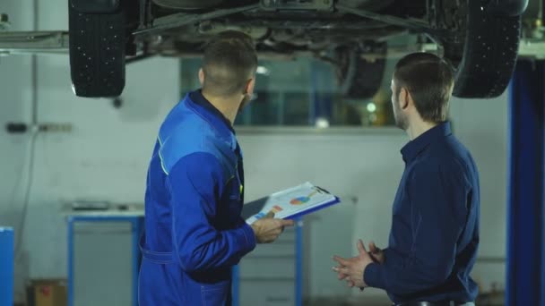 Mecánico de automóviles y dueño del coche. Confiado mecánico auto explicando algo a — Vídeos de Stock