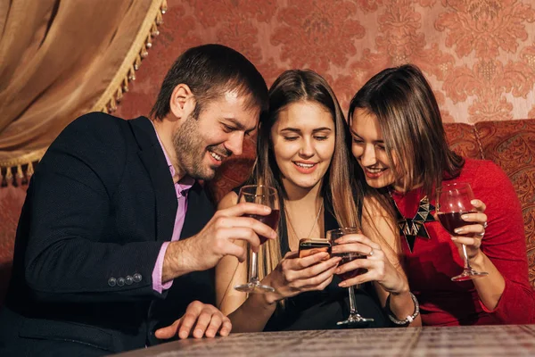 Two cute women and a man sitting in  restaurant  use the phone — Stock Photo, Image