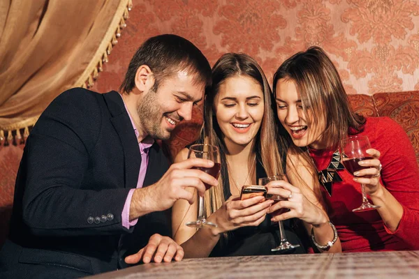 Dos mujeres lindas y un hombre sentado en el restaurante usar el teléfono — Foto de Stock