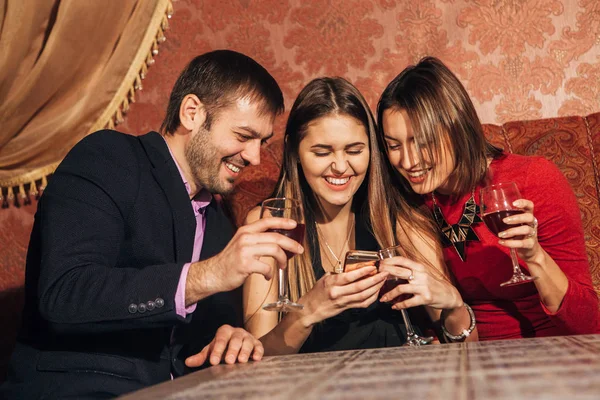Two cute women and a man sitting in  restaurant  use the phone — Stock Photo, Image