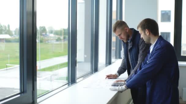 Fröhlicher junger Polier zeigt dem Architekten die Probleme des Bauens — Stockvideo