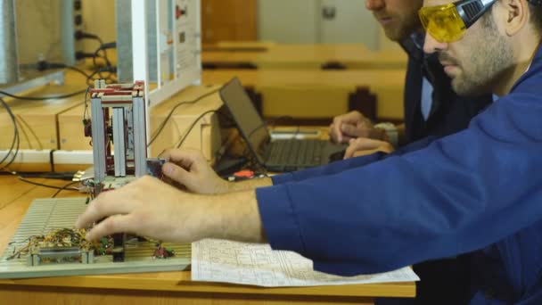 Νέοι μηχανικοί εργάζονται στο εργαστήριο και χρησιμοποιώντας έναν υπολογιστή — Αρχείο Βίντεο