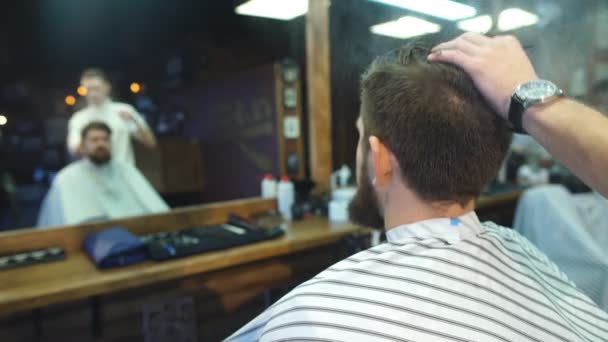 Joven barbudo hombre consiguiendo corte de pelo por peluquería mientras sentado en silla en barbería — Vídeos de Stock