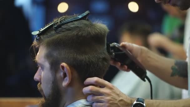 Создаю новый прическу. Молодой бородатый мужчина стрижется у парикмахера, сидя в кресле в парикмахерской — стоковое видео