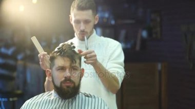Genç yakışıklı berber berber dükkanında sakallı çekici bir adamın saçını kesiyor.