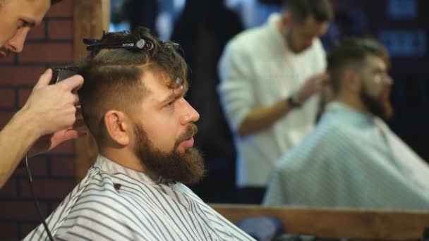 Maestro corta el pelo y la barba de los hombres en la peluquería, peluquería hace peinado para un hombre joven — Vídeo de stock
