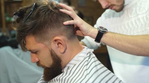 Barbeiro masculino em camisa xadrez pentear o cabelo de um cliente masculino na barbearia — Vídeo de Stock