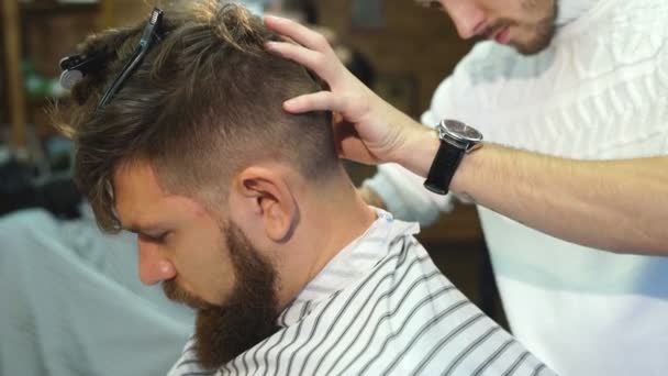 Peluquero masculino en camisa a cuadros peinando el cabello de un cliente masculino en la barbería — Vídeo de stock