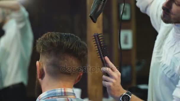 Barbeiro desigual está secando o cabelo de sua capa de cabelo cliente na barbearia . — Vídeo de Stock