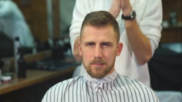 Alegre barbero hábil haciendo un corte de pelo con tijeras a un joven barbudo — Vídeos de Stock