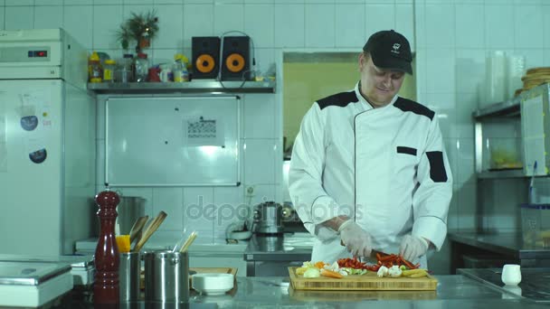 Verduras en tabla de cortar y detalle de las manos del chef, cocina del restaurante en el fondo — Vídeo de stock