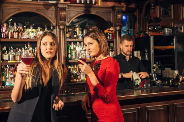 Две подруги в баре, чтобы выпить и поговорить. Женщина с речами рядом с ухом друга — стоковое фото