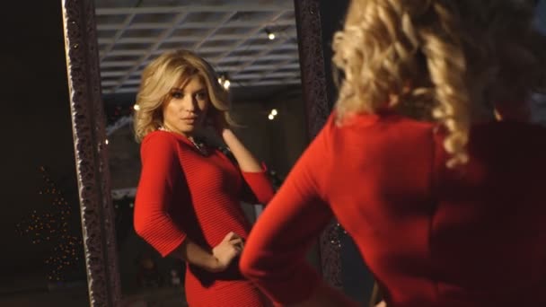 Vacker blondin i röd klänning poserar i spegeln och leende — Stockvideo
